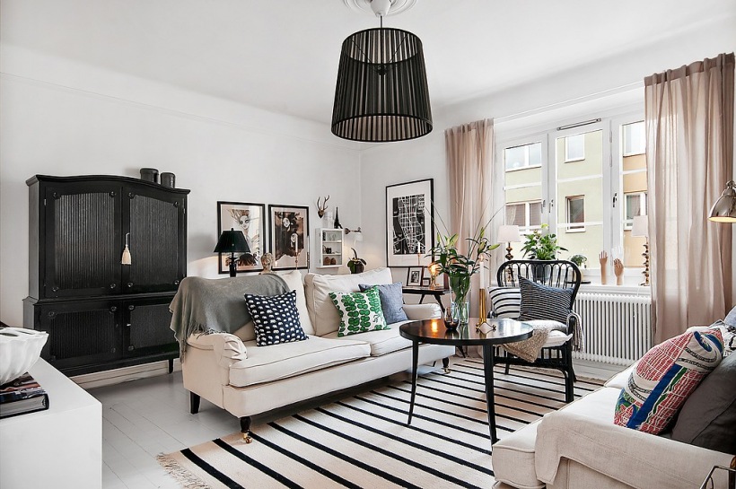 Czarna stylowa komoda z nadstawką,biały dywan w czarne paski,czarny stolik kawowy,graficzne wzory dekoracyjnych poduszek na jasnoszarej sofie w salonie