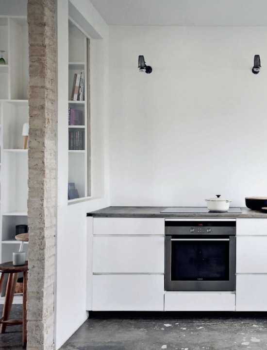 Minimalistyczna aranżacja białej kuchni z surową cegłą i betonową posadzką