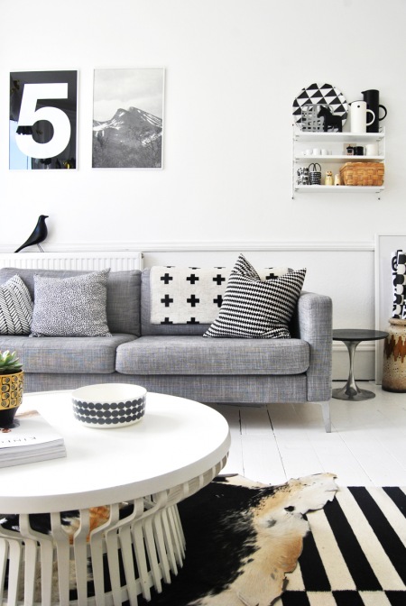 Skandynawski salon z szarą sofą,białą podłogą i grafikami na ścianie