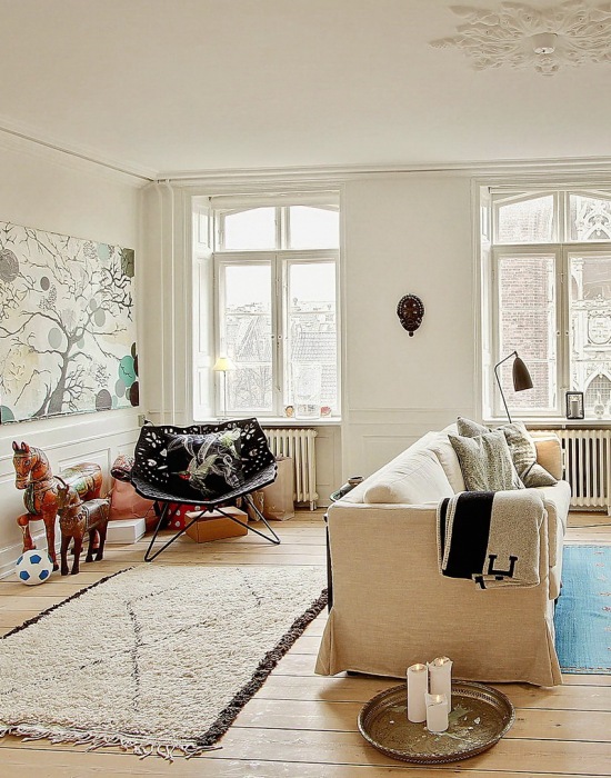 Nowoczesne obrazy,naturalne drewno,tkane dywany i proste witryny w skandynawskim salonie
