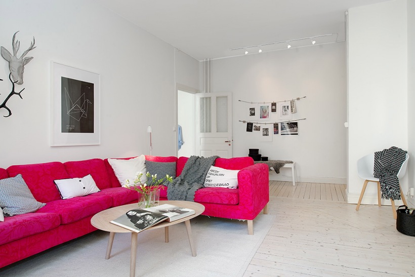 Rózowy narożnik,drewniany owalny stolik,biało-czarne fotografie i grafiki na ścianie w salonie skandynawskim