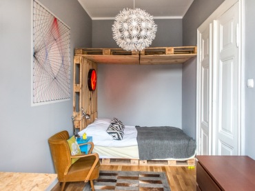 Najbardziej charakterystycznym elementem wystroju sypialni jest łóżko z palet. To nie tylko rama, ale cała konstrukcja, która sięga sufitu. Drewniane akcenty ocieplają eklektyczne...