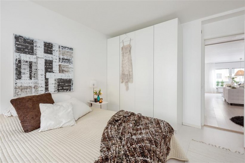 Biała szafa,nowoczesny obraza,brązowa poduszka i beżowa narzuta na łóżko
