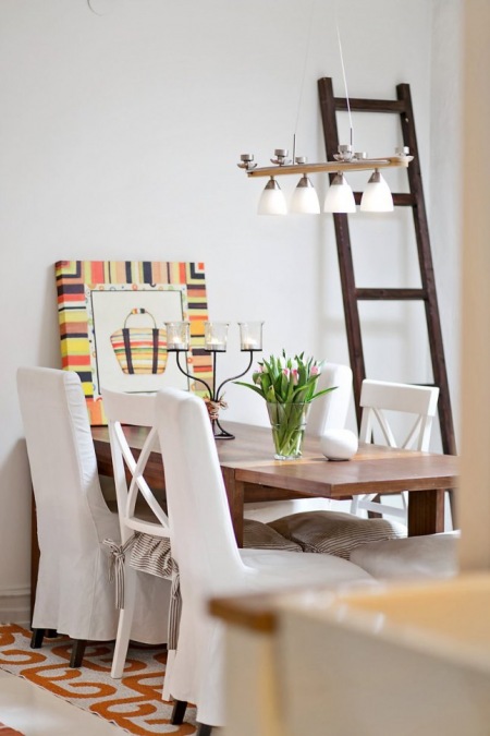 Krzesła w ubrankach,drewniana drabina i brązowy stół w jadalni