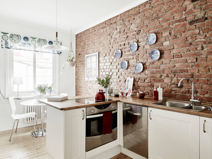 Skandynawska kuchnia z białymi szafkami z drewnianymi blatami i ścianą z czerwonej cegły