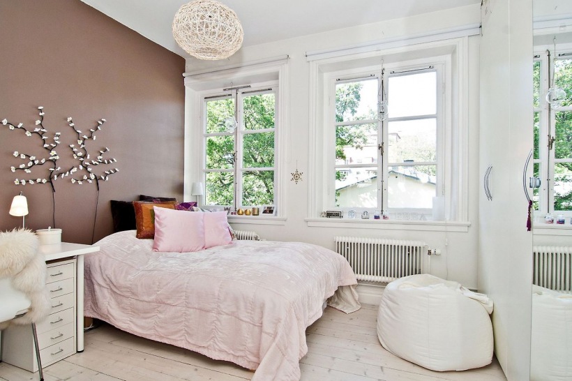 Beżowo-brązowa ściana w bialej sypialni skandynawskiej z różowymi, brązowymi i czarnymi poduszkami