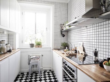 Biało-czarna terakota ułożona w karo na podłodze w białej kuchni z drewnianymi blatami na szafkach (25980)