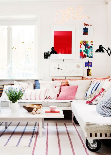 Czerwone, różowe i niebieskie poduszki dekoracyjne na sofie i kolorowe plakaty na ścianie