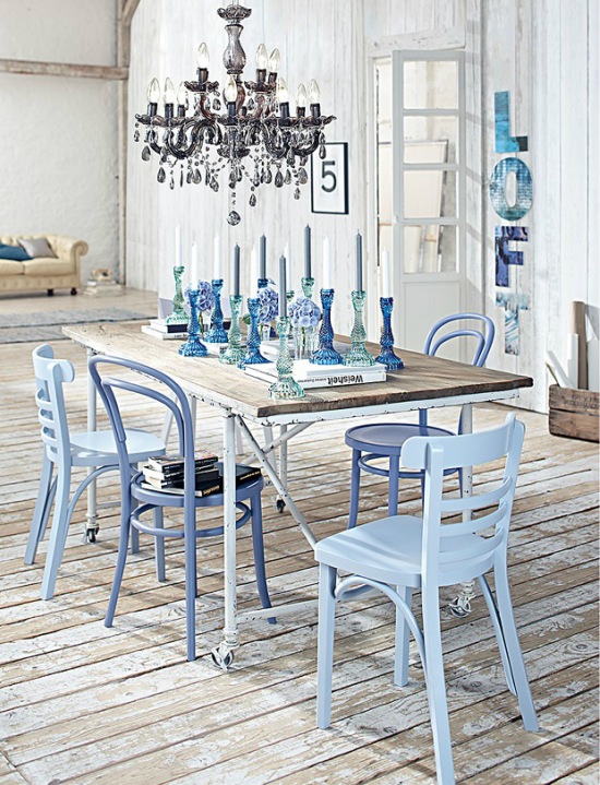 Patynowana i bielona podłoga z desek,metalowy stół biały z drewnianym blatem i niebieskimi świecznikami,błękitne i białe krzesła skandynawskie