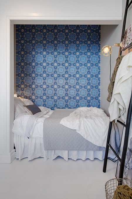 Łóżko we wnęce, czyli alkowa w skandynawskim stylu z  tapetą  z niebieskim ornamentem
