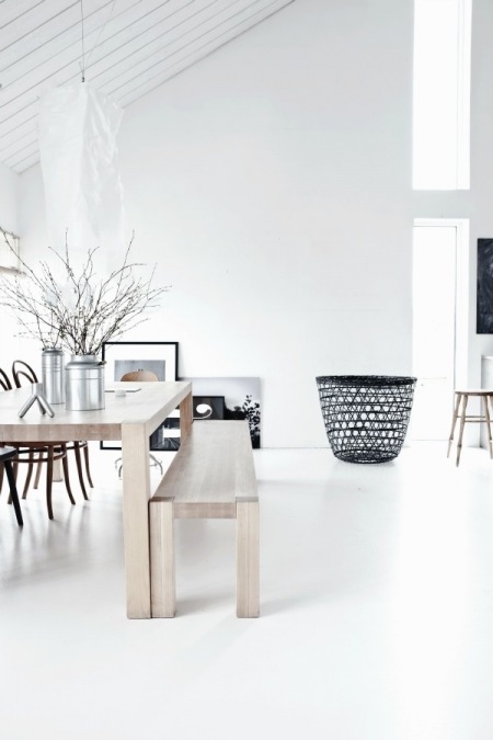 Biały salon, drewniany stół w naturalnym kolorze i ażurowy czarny kosz