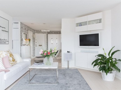 Szary dywan,kwadratowy stolik na chromowanych nogach,biała sofa z różowo-pudrowymi poduszkami w otwartym salonie (28629)