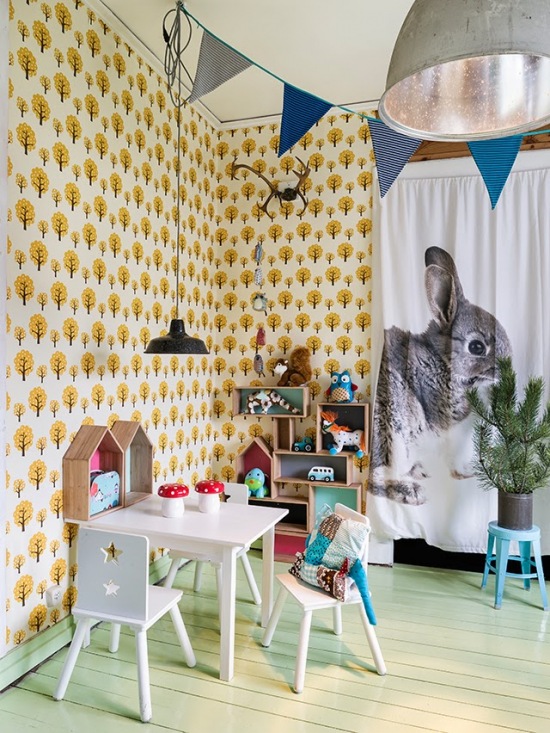 Miętowy kolor desek na podłodze w pokoju dziecięcym, z tapetą w żółto-czarne drzewka,niebieskimi proporczykami i zasłonami z królikami