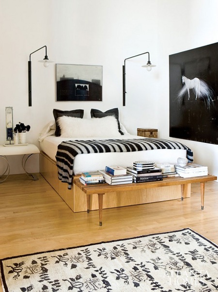 Czarne kinkiety, pościel  i fotografie w białej sypialni z drewnianym łóżkiem