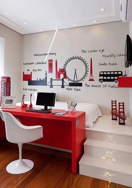 Czerwone biurko, białe krzesło nowoczesne,białe schodki na podest z łóżkiem i czarno-czerwone naklejki w londynskim klimacie na ścianie w pokoju dla chłopca