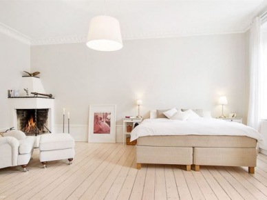 Beżowe tapicerowane łóżko,podłoga z naturalnych desek,fotel z podnóżkiem na kółkach w sypialni z murowanym kominkiem (27744)