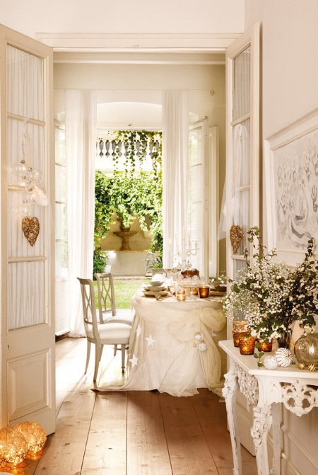 Szerokie deski z naturalnego drewna na podłodze,białe francuskie krzesła,białe drzwi z dekoracyjna firanką i świąteczne dekoracje w stylowej  jadalni