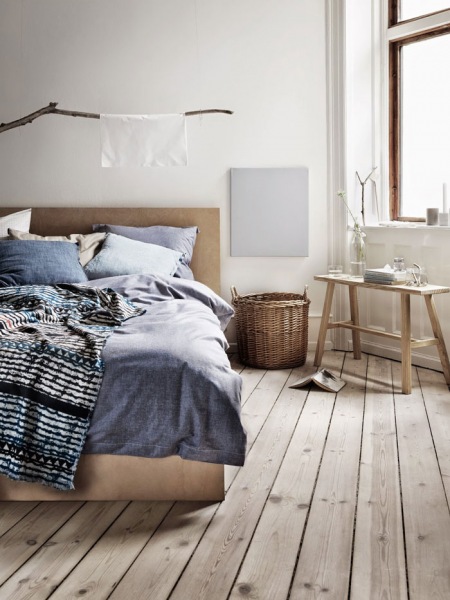 Podłoga z drewnianych sosnowych desek,wiklinowy kosz,drewniana ławka skandynawska,drewniane łóżko,niebieska pościel z lnu