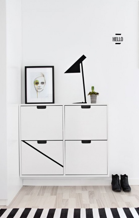 Biała wisząca szafka na buty,skandynawskie ilustracje,czarna lampka stołowa w nowoczesnym stylu w aranzacji przedpokoju w stylu skandynawskim