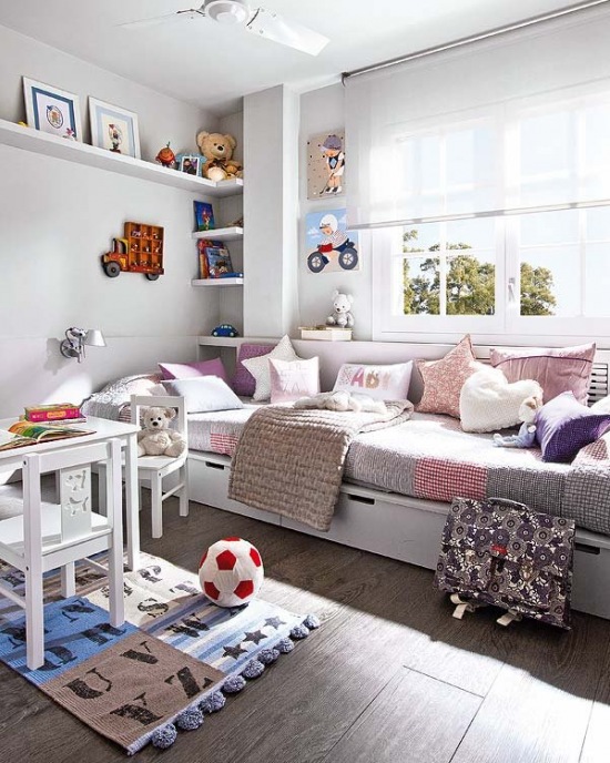 Białe łóżko z szufladami, różowymi i fioletowymi poduszkami w pokoju dziecięcym z półkami i białymi mebelkami