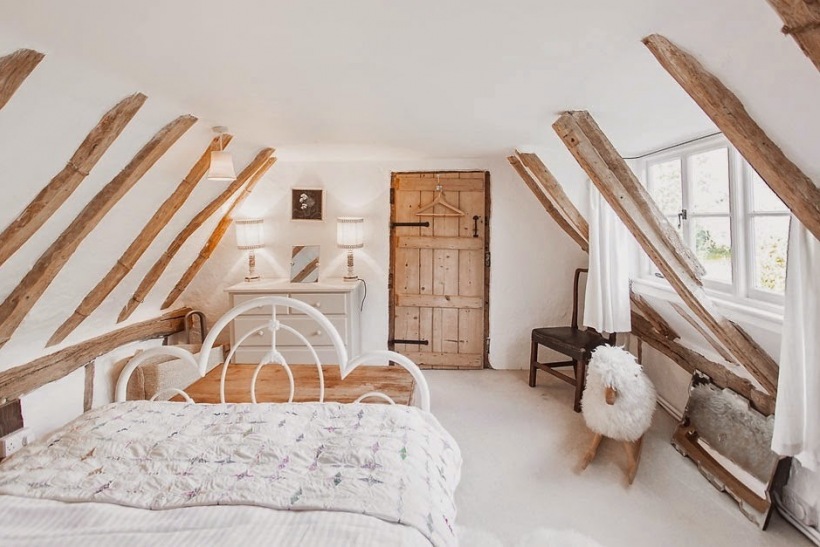 Drewniane wiejskie wrota w aranżacji sypialni z białym kutym łóżkiem na poddaszu