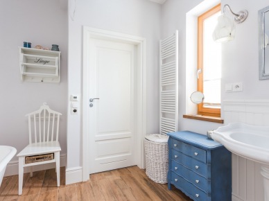 Biała łazienka z niebieskimi dodatkami. Podłoga imitująca drewno oraz wiklinowe dekoracje dodają jej uroku i ocieplają całe...