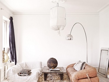 Lampa kokon z drutu i bawełny,skórzana sofa desingerska z zapięciami bocznymi,dywan futrzak,lampa podłogowa srebrna i gliniany wazon na drewnianej ławie (27390)