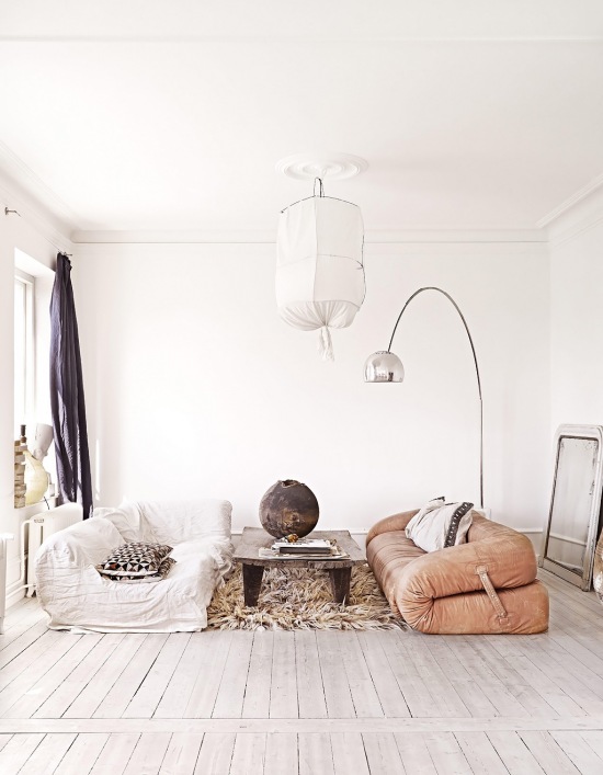 Lampa kokon z drutu i bawełny,skórzana sofa desingerska z zapięciami bocznymi,dywan futrzak,lampa podłogowa srebrna i gliniany wazon na drewnianej ławie