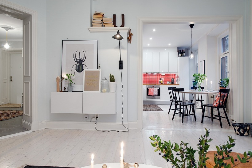 Otwarty salon z jadalnią i kuchnią w stylu skandynawskim z wiszącą szafką z grafikami i biała podłogą z desek