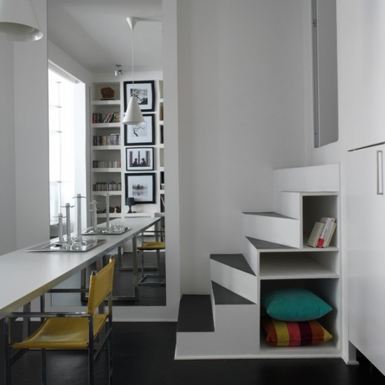 Biała i nowoczesna  jadalnia z dużym lustrem na ścianie i pomysłowych schodach ze schowkami