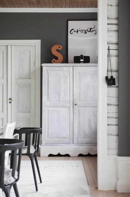 Czarne ściany z białymi listwami,drewniany dufit,bielone przecierane szafy i czarnegiete  krzesła skandynawskie