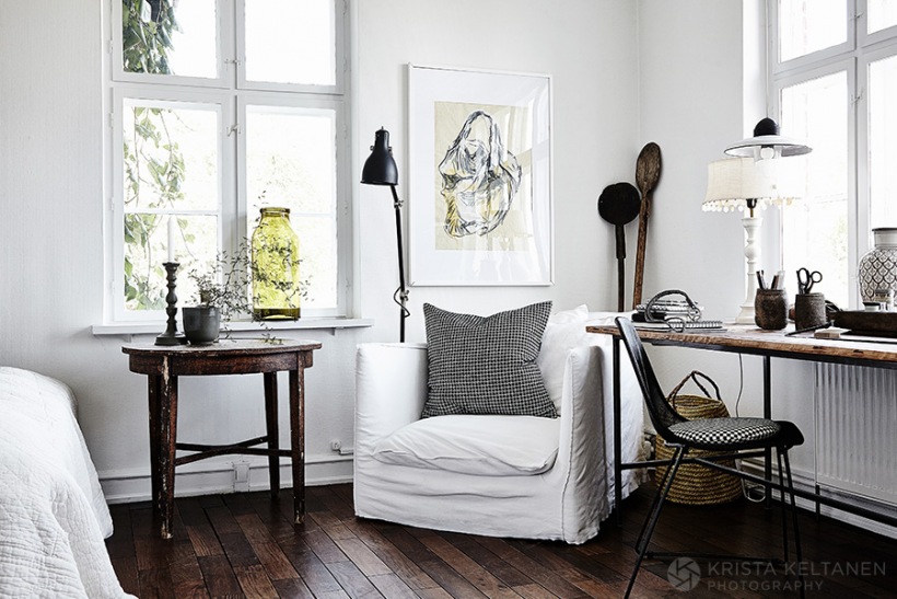 Biały fotel w spranej bawełnie,drewniany rustykalny stolik,ciemnobrązowa podłoga z drewna,plakaty i industrialne lampki i konsola-biurko