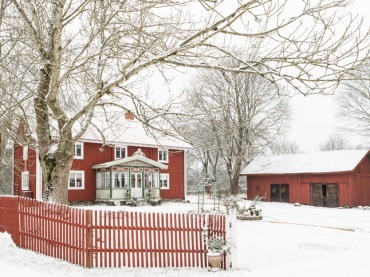 Czerwony dom otulony bielą śniegu wprowadza w świąteczny nastrój. Rustykalny krajobraz posiadłości na wsi podkreśla nie...