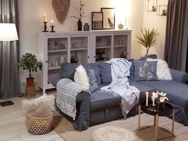 Na szarej sofie leżą koce i poduszki, które podkreślają ciepły charakter salonu. Ustawiona pod ścianą witryna pozwala...