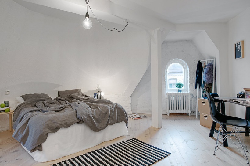 Skośna ściana z białej cegły w skandynawskiej sypialni na poddaszu