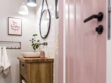 Łazienka jest urządzona w stylu skandynawskim, który widać np. po dobranych lampach. Ciekawym elementem wystroju są pastelowe drzwi w różowym...