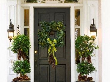 Czarne kinkiety przy czarnych drzwiach z czarnymi gazonami z zielonymi drzewkami i szyszkami i zielony wianek na drzwiach w świątecznej dekoracji wejścia do domu (27398)
