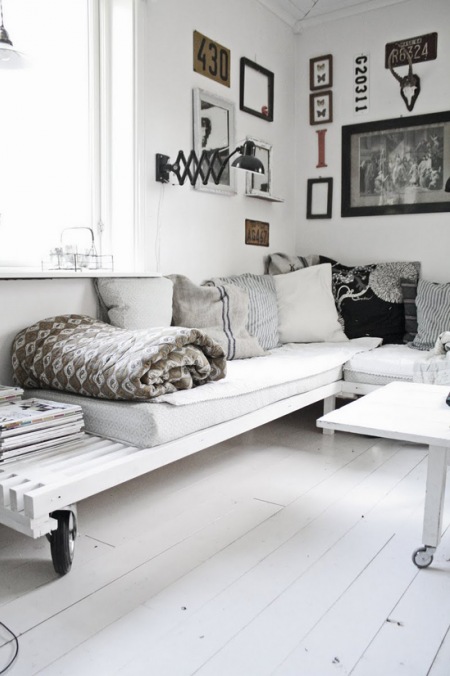 Biała sofa z palet na kółkach, czarny kinkiet z wysiegnikiem z galerią grafik i fotografii