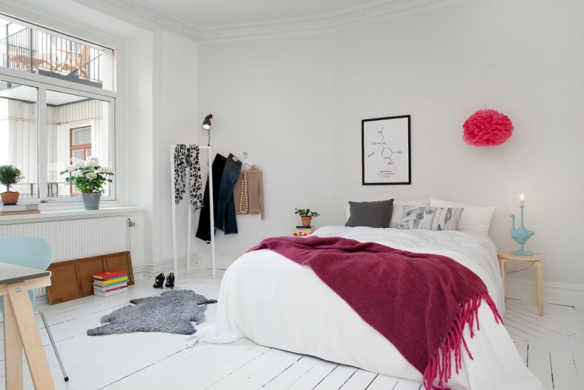 Różowa narzuta i różowy pompon w dekoracji białej sypialni skandynawskiej