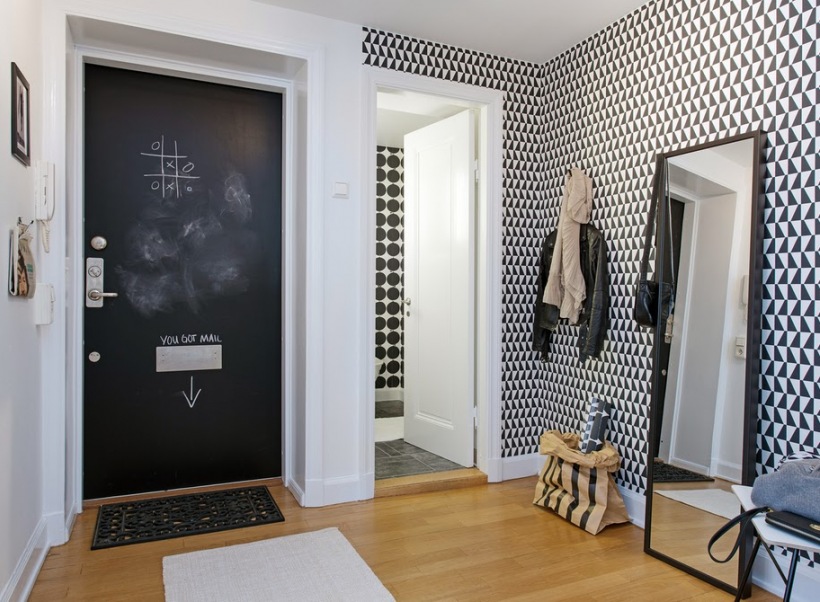 Biało-czarne tapety w geometryczne wzory,drzwi pomalowane farbą tablicową,duże stojące lustro podłogowe w czarnych ramach