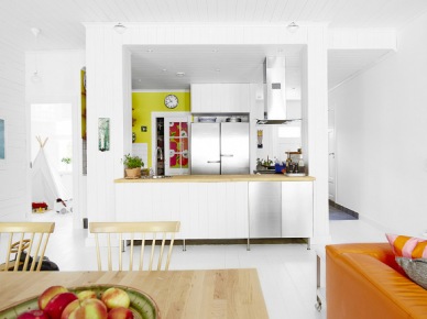 Biala kuchnia z drewnianymi blatami i żółtą ścianą w otwartym widoku na jadalnię i salon (24656)