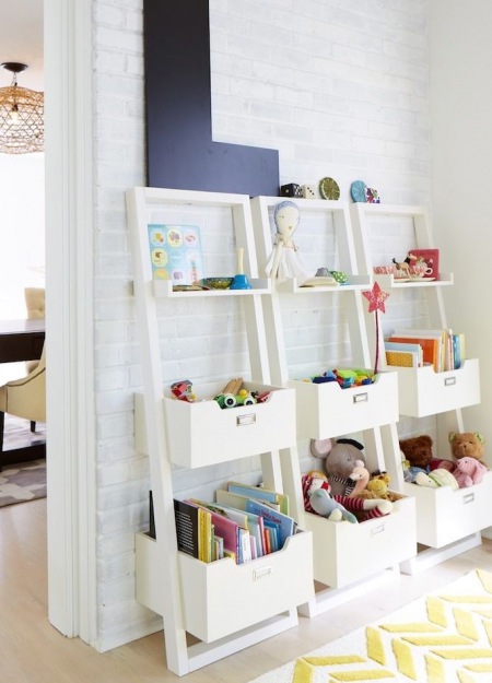 Białe drabinki z pojemnikami na dziecięce zabawki przy ścianie z białej cegły
