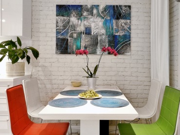 Ściana z białej cegły, nowoczesny obraz na ścianie przy białym stole z kolorowymi krzesłami w jadalni (28202)