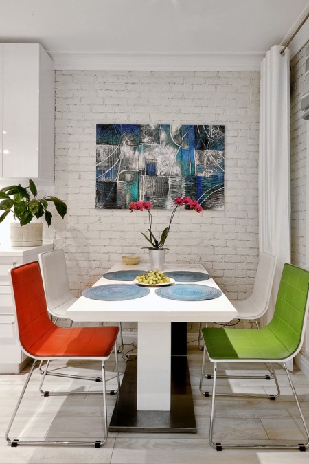 Ściana z białej cegły, nowoczesny obraz na ścianie przy białym stole z kolorowymi krzesłami w jadalni