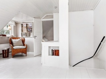 Rattanowy duży fotel z poduszkami,półka na czasopisma na ścianie na białym poddaszu w skandynawskim domku (27875)