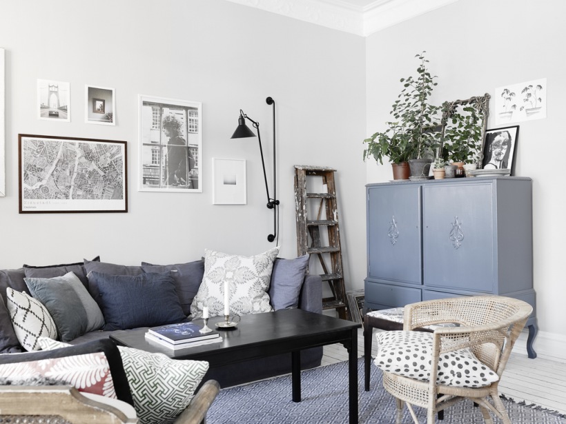Niebieska szafa w stylu orientalnym,szara sofa nowoczesna,czarny kinkiet na ramieniu,rattanowy fotel w eklektycznym salonie