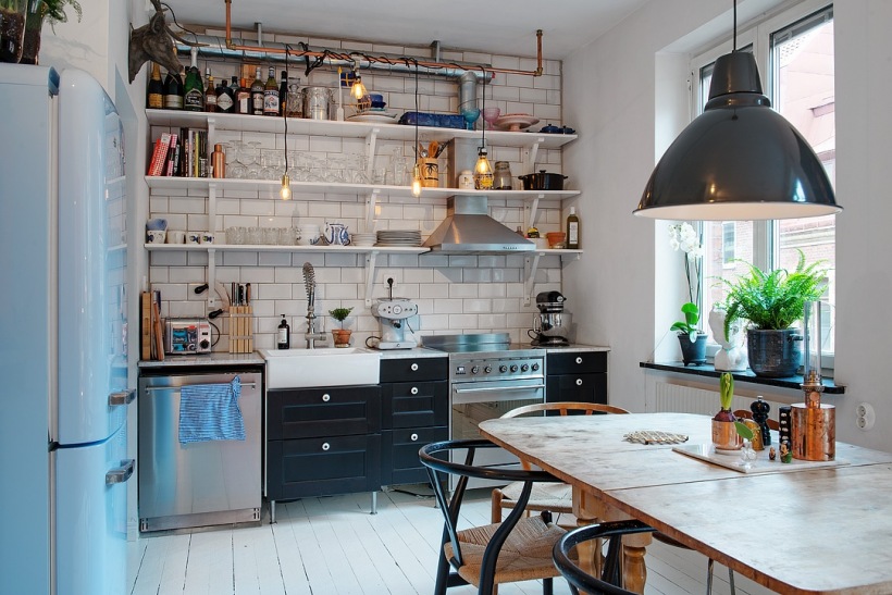 Industrialna kuchnia z odkrytymi półkami na ścianie, białą podłogą z desek,drewnianym stołem i czarną metalową lampą