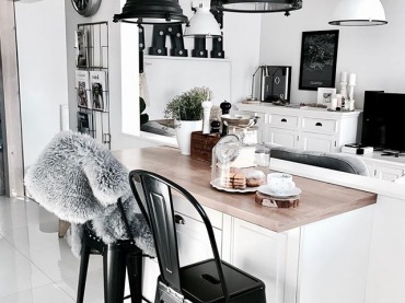Aranżacja kuchni i całego pokoju dziennego bazuje na spokojnej bieli. Urozmaicają ją czarne dodatki, np. w postaci charakterystycznych lamp nad kuchennym blatem śniadaniowym. Takie wyraziste elementy zdecydowanie wpływają na niepowtarzalny charakter...