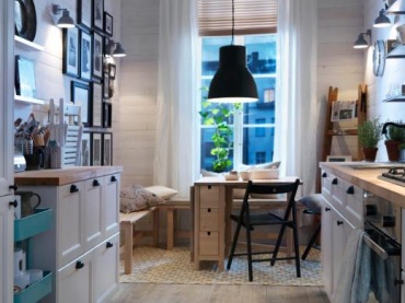 Ikeowska kuchni w bieli z jasną drewnianą podłogą.Jest też galeria na ścianie i czarna lampa nad stołem prze co tworzy...