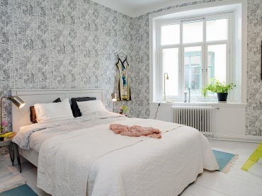 Szaro-biała drukowana tapeta  na scianie w sypialni,białe łóżko ,szary taboret i srebrna lampka nocna (25898)